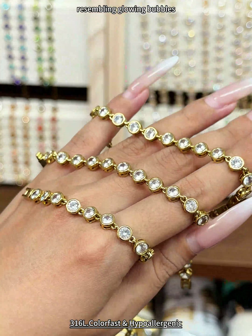 Gold-tone tennis bracelet with round clear stones in bezel-style settings, shown by hand for wholesale jewelry buyers.