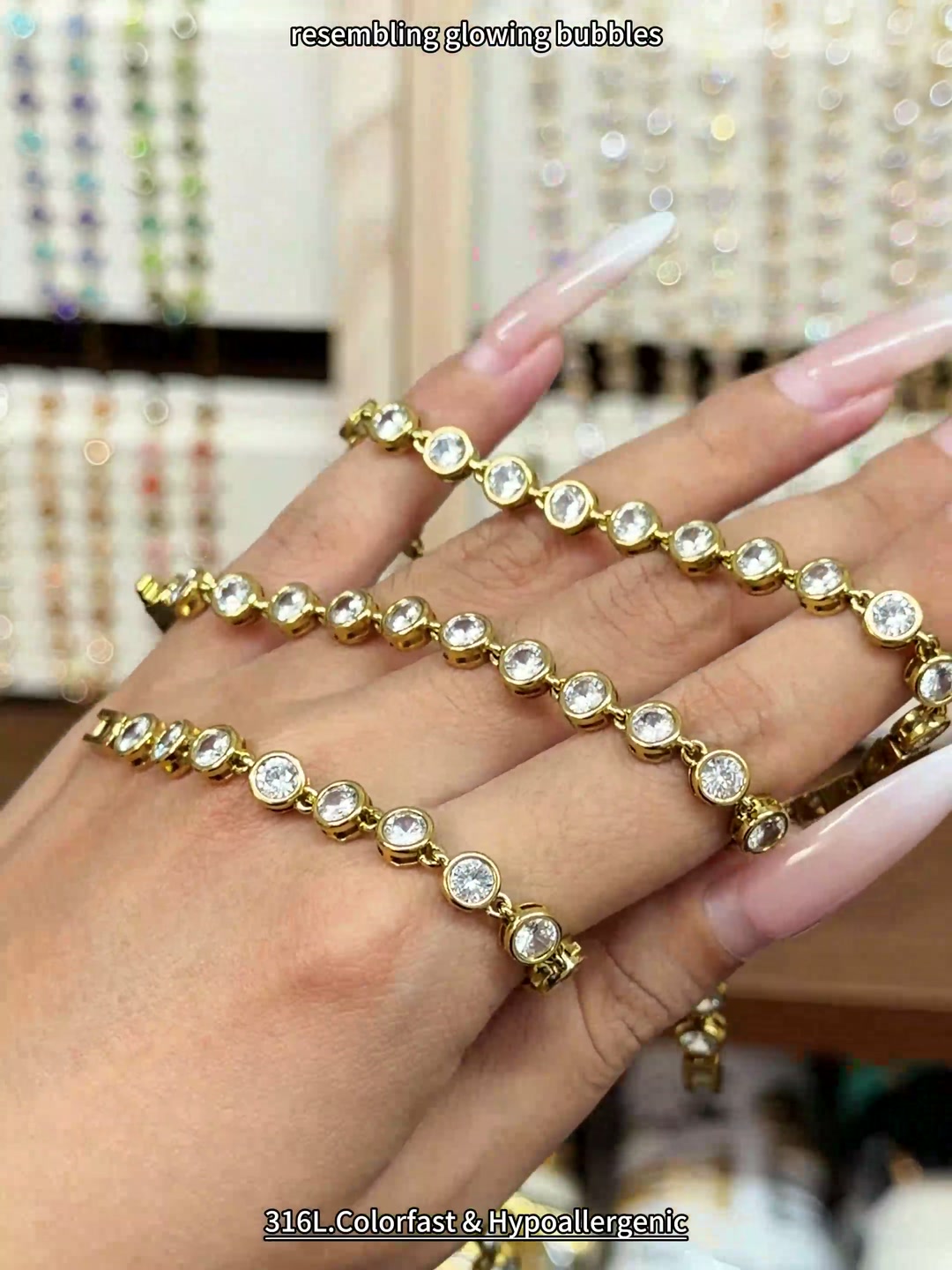 Gold-tone tennis bracelet with round clear stones in bezel-style settings, shown by hand for wholesale jewelry buyers.