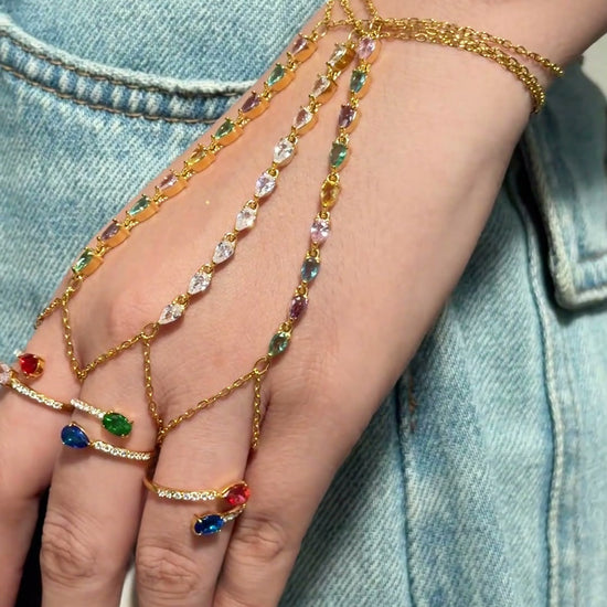 Gold-tone hand chain jewelry with multicolored stones and delicate chains connecting the wrist to the fingers.