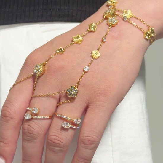 Gold-tone hand chain bracelets with floral motifs and clear stone accents, shown on a model's hand.