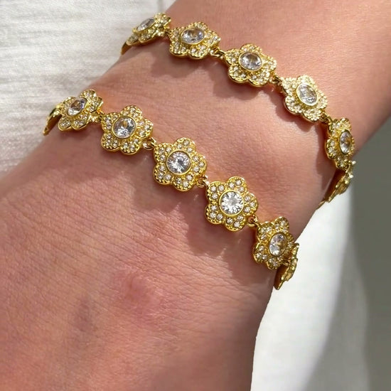 Gold-tone floral link bracelets with clear sparkling centers shown stacked on the wrist.