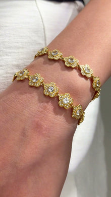 Gold-tone floral link bracelets with clear sparkling centers shown stacked on the wrist.