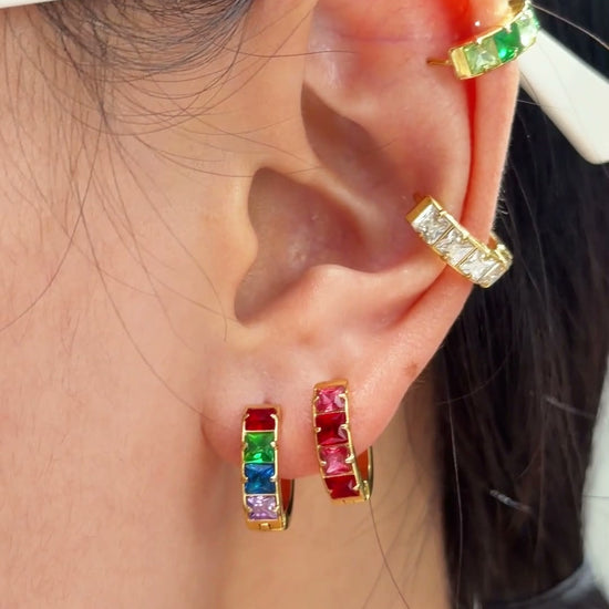 Gold-tone hoop earrings with colorful rectangular stones in rainbow and pink tones, shown on a model's ear.