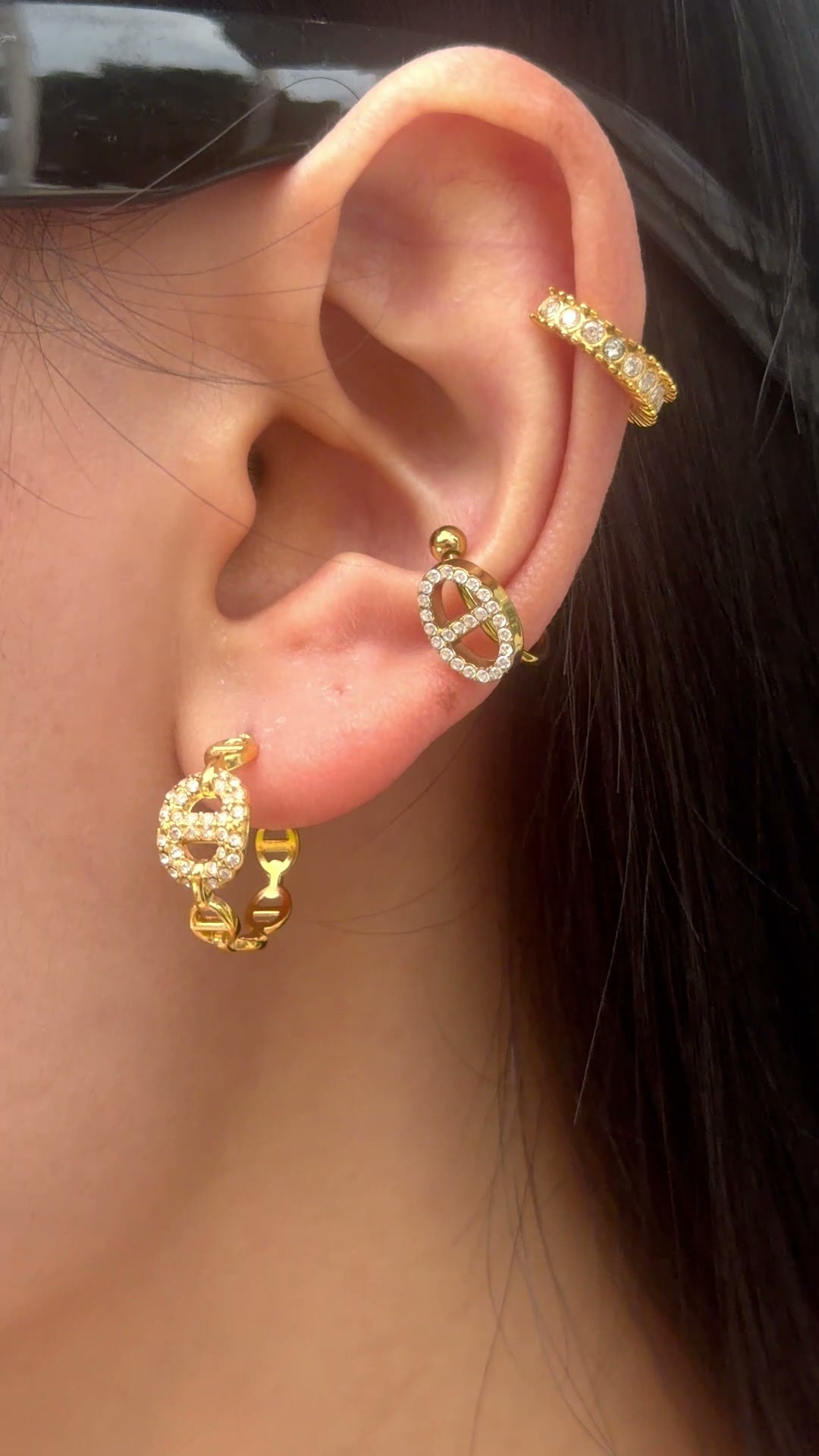 Gold-tone hoop earrings with oval link details and clear stone accents, shown on a model.