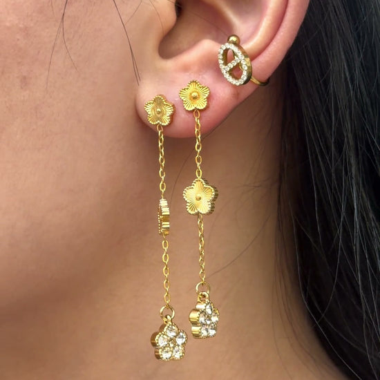 Long gold-tone chain earrings with flower motifs and clear stone floral drops, shown on a model.