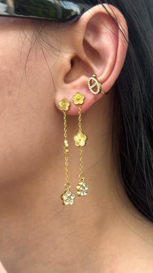 Long gold-tone chain earrings with flower motifs and clear stone floral drops, shown on a model.