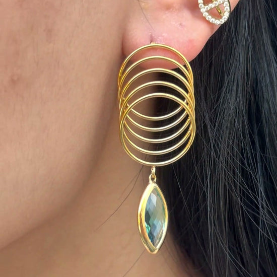 Gold-tone overlapping circle drop earrings with a marquise-shaped blue-green stone, shown on a model.