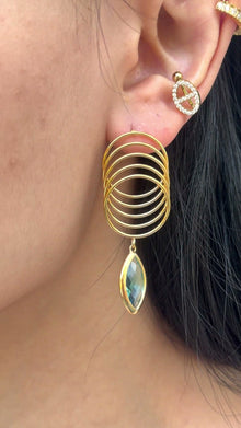 Gold-tone overlapping circle drop earrings with a marquise-shaped blue-green stone, shown on a model.