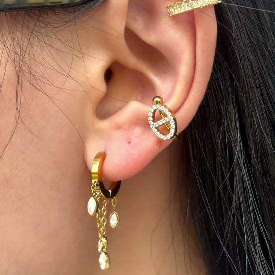 Gold-tone small hoop earrings with dangling chains and marquise-shaped clear stones, shown on a model.