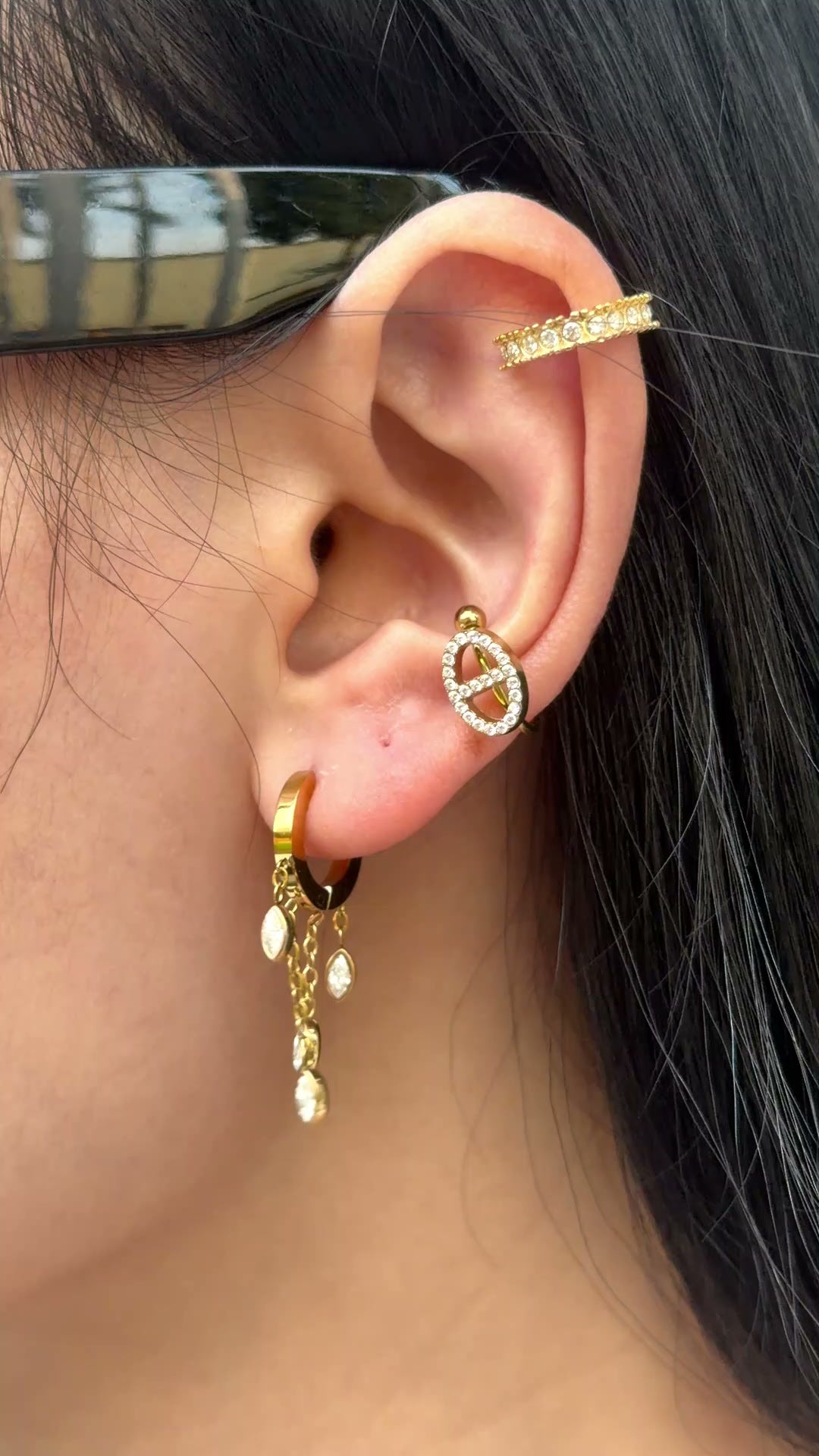 Gold-tone small hoop earrings with dangling chains and marquise-shaped clear stones, shown on a model.