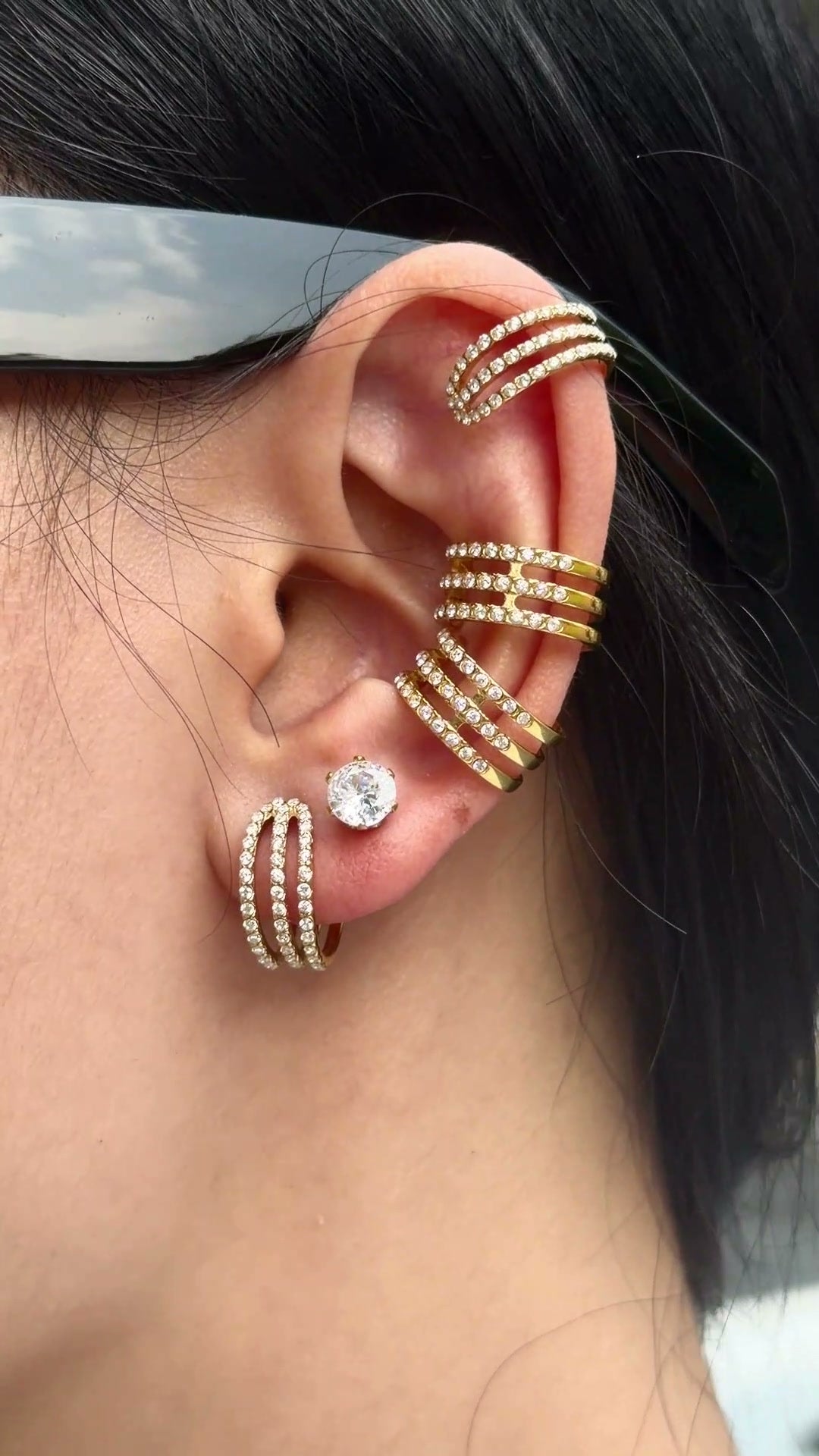 Gold-tone triple-row ear cuffs and hoop earrings with clear stone accents, shown on a model.