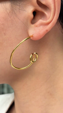 Gold-tone open hoop earrings with curled ends, shown on a model.