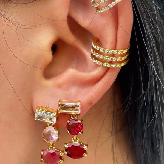 Gold-tone drop earrings with rectangular, round and oval pink and red stones, shown on a model.