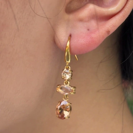 Gold-tone drop earrings with three champagne-colored stones in mixed shapes, shown on a model.