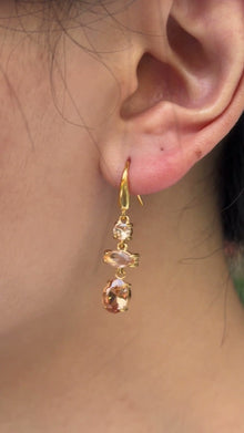 Gold-tone drop earrings with three champagne-colored stones in mixed shapes, shown on a model.