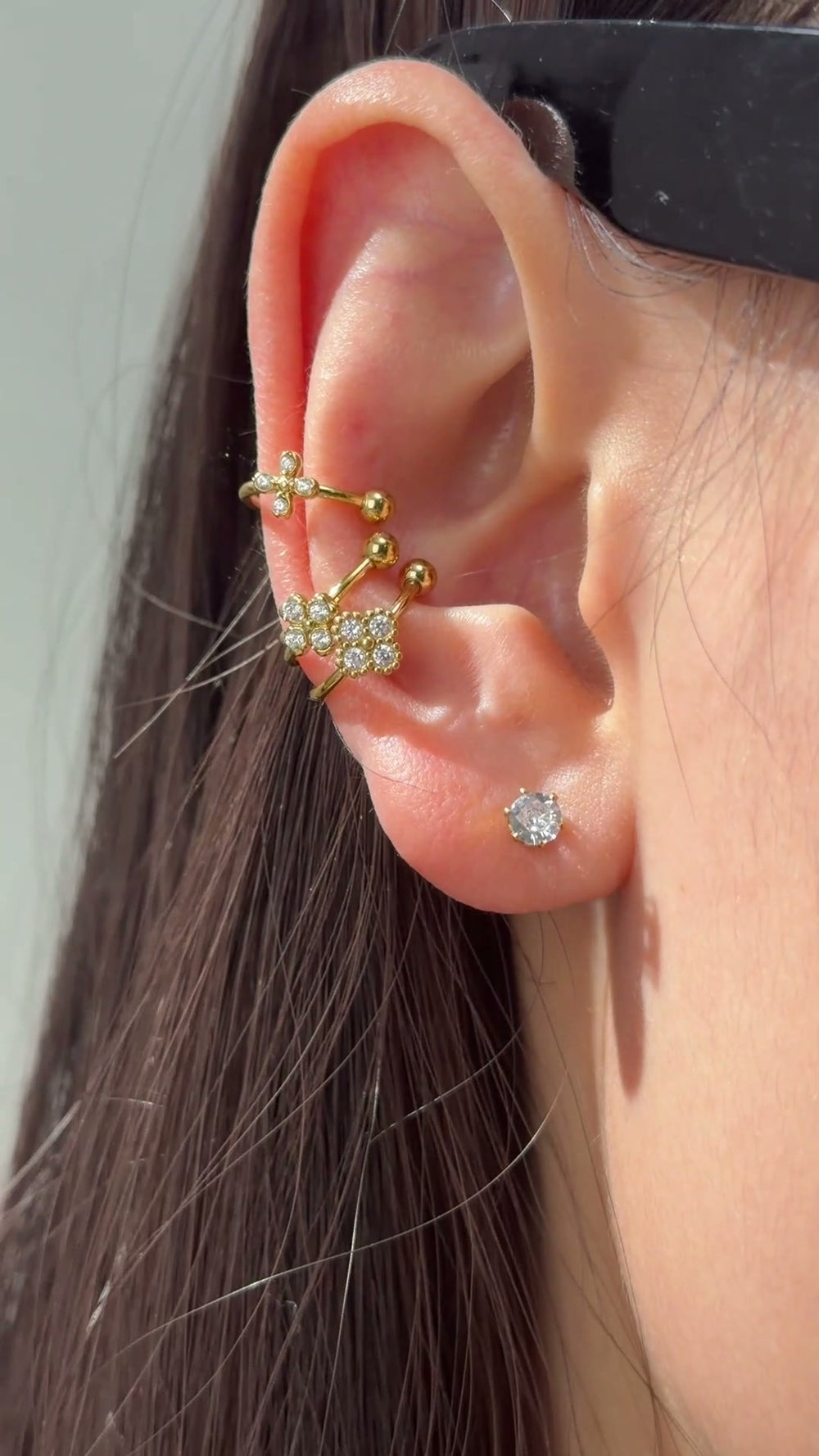 Gold-tone ear cuffs with delicate floral details and clear sparkling stones shown on the ear.