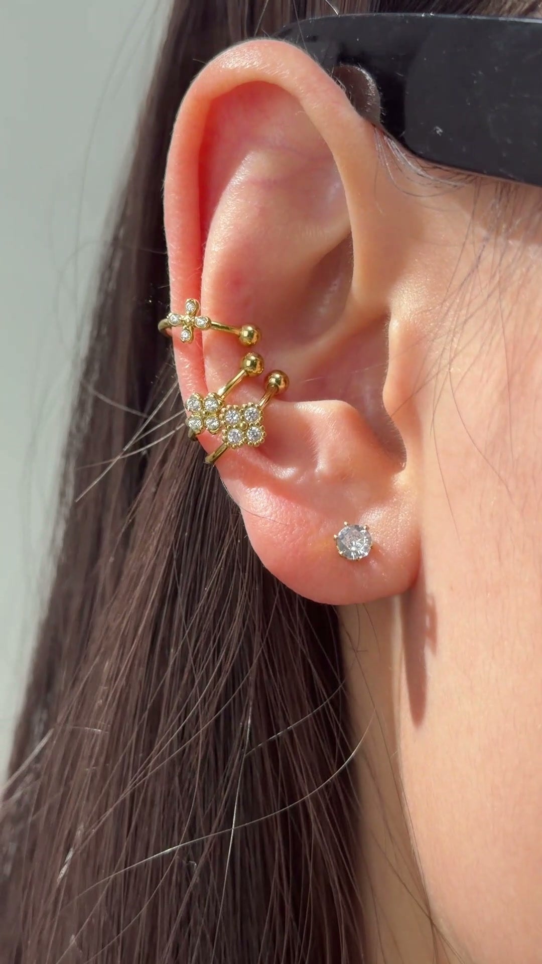 Gold-tone ear cuffs with delicate floral details and clear sparkling stones shown on the ear.