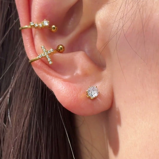 Slim gold-tone ear cuffs with clear stone accents and polished ball ends styled along the ear.