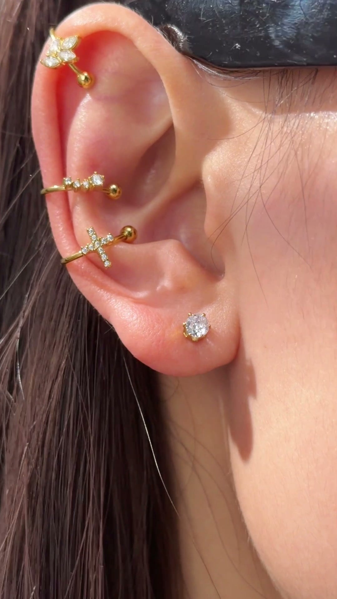 Slim gold-tone ear cuffs with clear stone accents and polished ball ends styled along the ear.