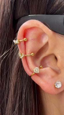 Gold-tone ear cuffs with clear heart-shaped and geometric stone details shown stacked on the ear.