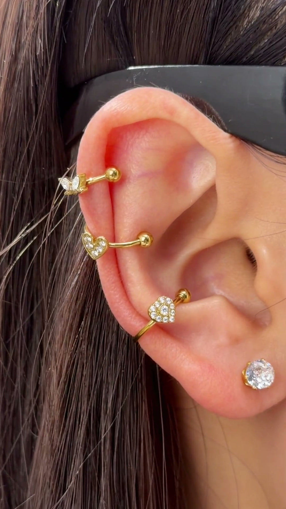 Gold-tone ear cuffs with clear heart-shaped and geometric stone details shown stacked on the ear.