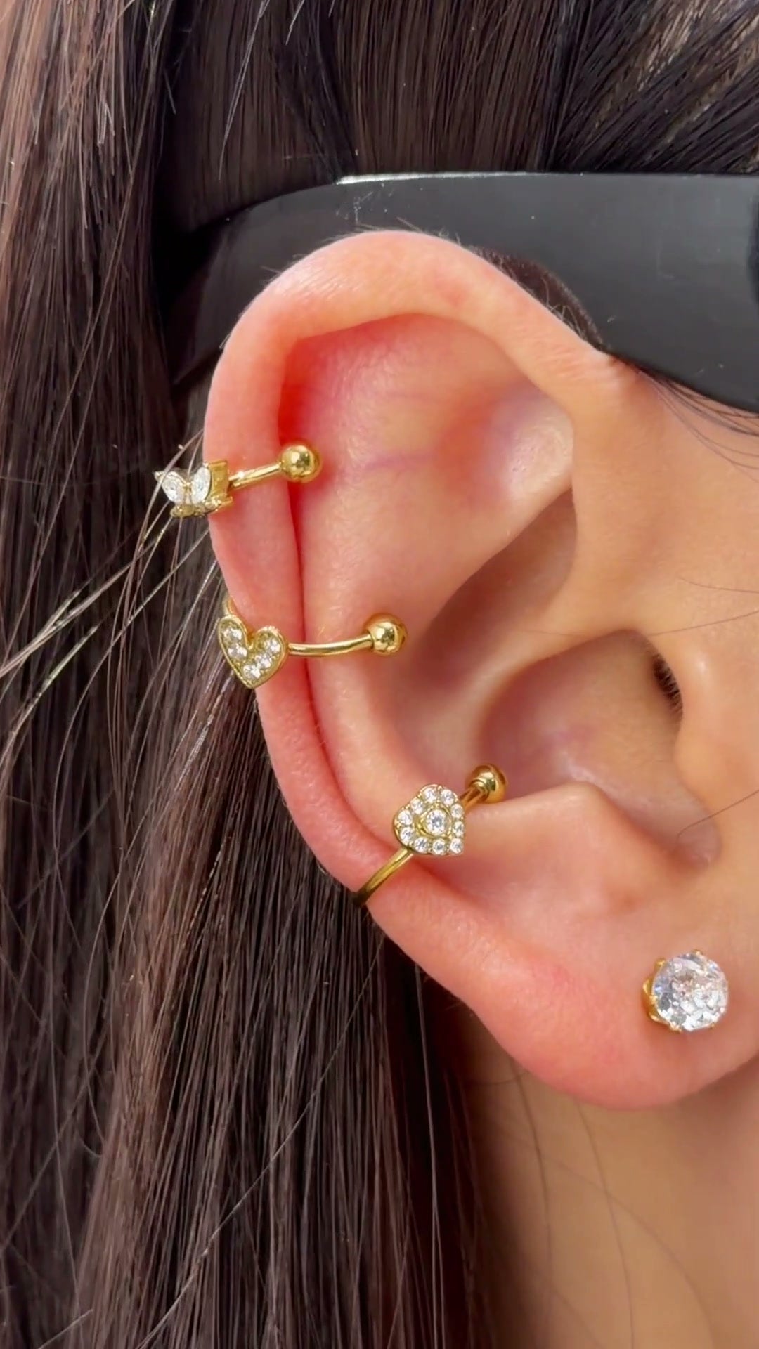 Gold-tone ear cuffs with clear heart-shaped and geometric stone details shown stacked on the ear.