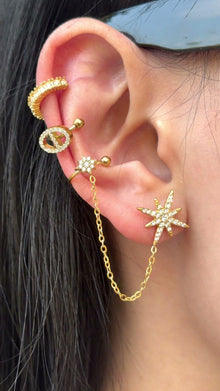 Gold-tone starburst stud and floral ear cuff connected by a chain, with clear stone accents, shown on a model.