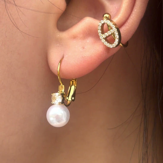 Gold-tone drop earrings with white pearl-like beads and clear stone accents, shown on a model.