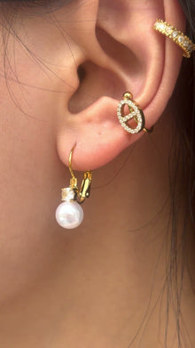 Gold-tone drop earrings with white pearl-like beads and clear stone accents, shown on a model.