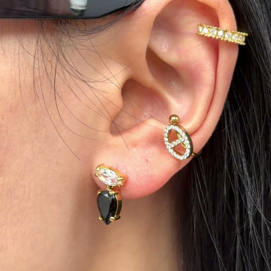Gold-tone earrings with clear marquise-shaped stones and black teardrop stones, shown on a model.