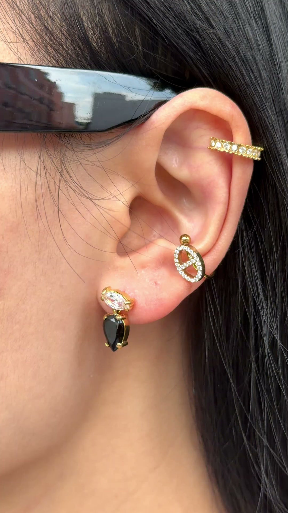 Gold-tone earrings with clear marquise-shaped stones and black teardrop stones, shown on a model.