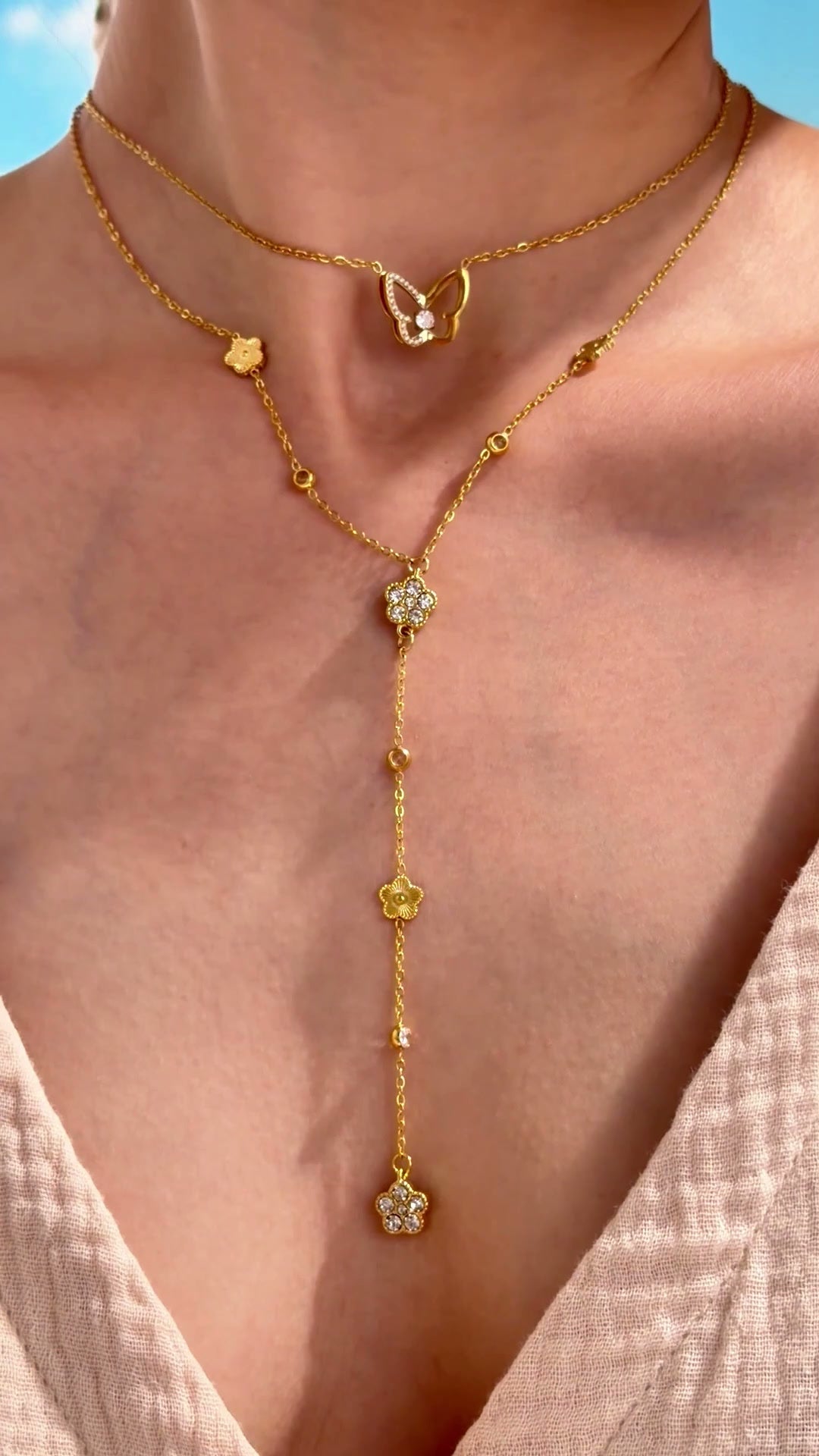 Layered gold-tone necklaces featuring a butterfly pendant and a floral Y-shaped lariat with clear stone accents, shown on a model.