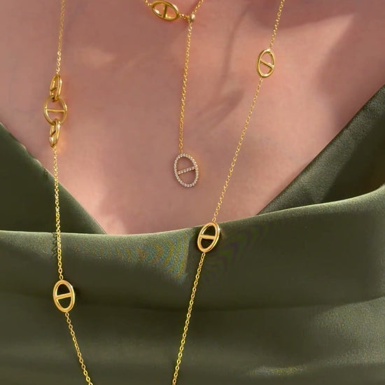 Layered gold-tone necklaces with oval mariner-link stations and clear-stone accents, styled with an olive-green satin top.