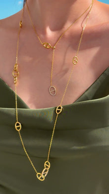 Layered gold-tone necklaces with oval mariner-link stations and clear-stone accents, styled with an olive-green satin top.