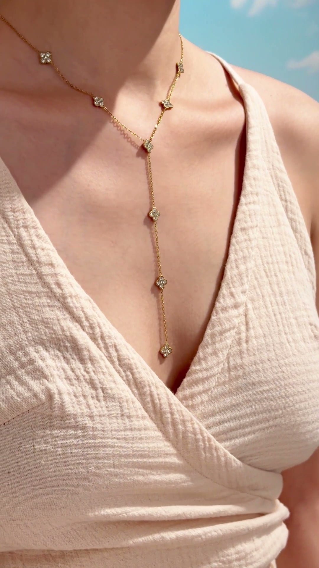 Gold-tone Y-shaped lariat necklace with clear-stone four-petal floral stations, shown on a model.