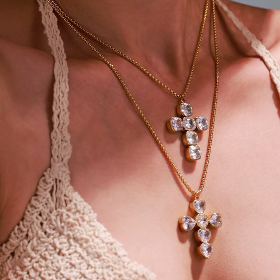 Model wearing layered gold-tone cross pendant necklaces with clear cushion-cut and heart-shaped stones.