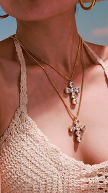 Model wearing layered gold-tone cross pendant necklaces with clear cushion-cut and heart-shaped stones.