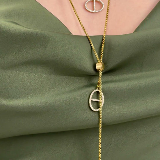 Layered gold-tone lariat necklaces with oval pendants and clear stone accents, styled on an olive-green satin top.
