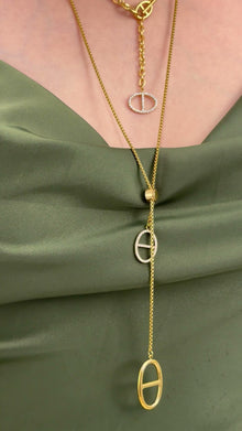 Layered gold-tone lariat necklaces with oval pendants and clear stone accents, styled on an olive-green satin top.