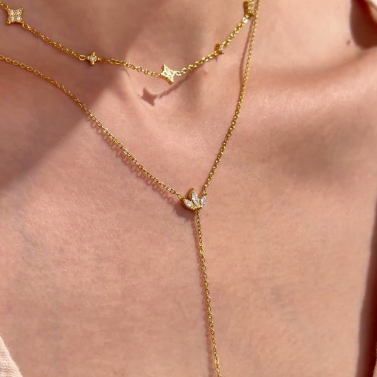 Layered gold-tone necklaces with four-point star stations and a leaf-shaped lariat pendant with clear stone accents, shown on a model.