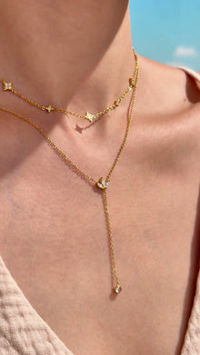 Layered gold-tone necklaces with four-point star stations and a leaf-shaped lariat pendant with clear stone accents, shown on a model.