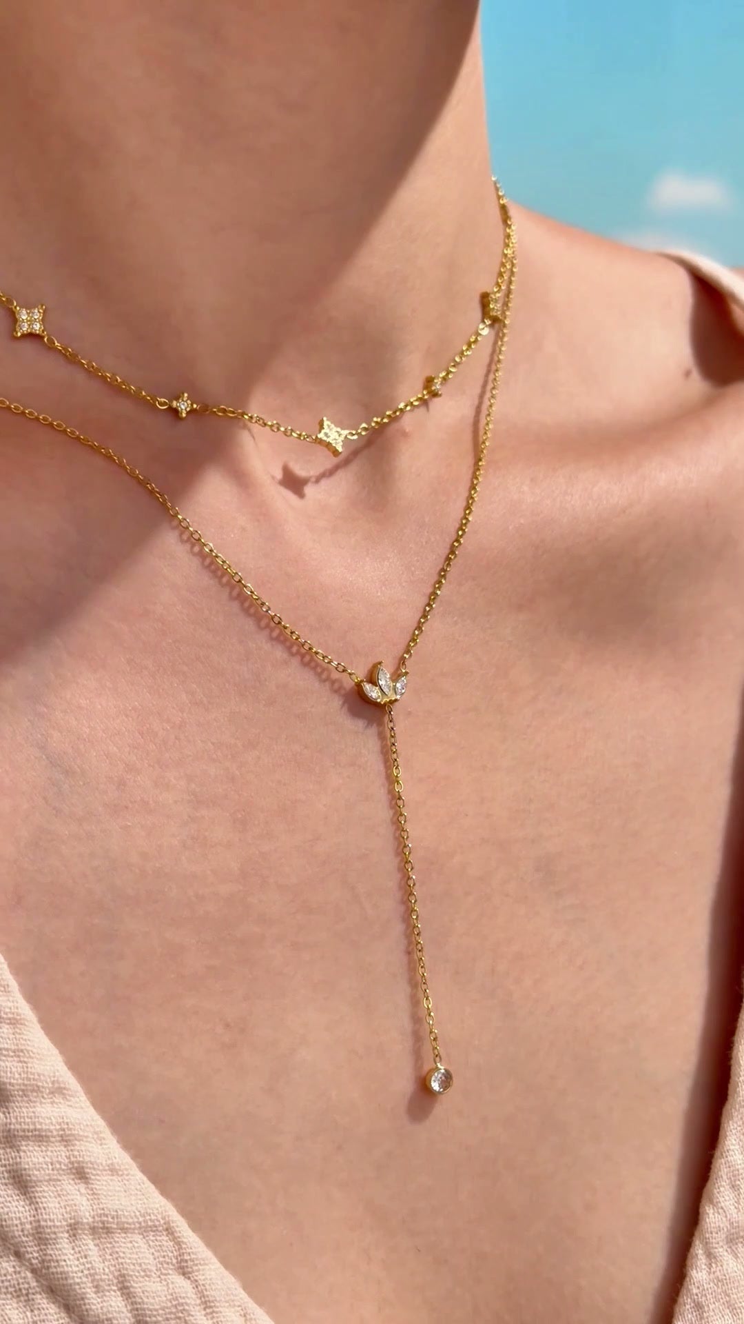 Layered gold-tone necklaces with four-point star stations and a leaf-shaped lariat pendant with clear stone accents, shown on a model.