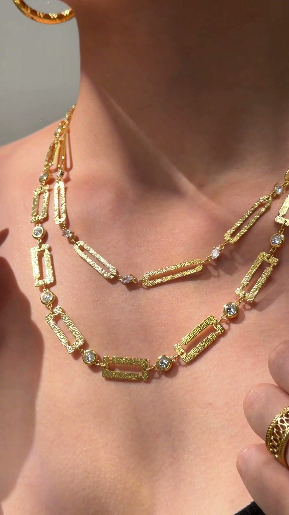 Layered gold-tone necklaces with textured rectangular links and clear sparkling accents shown on a model.