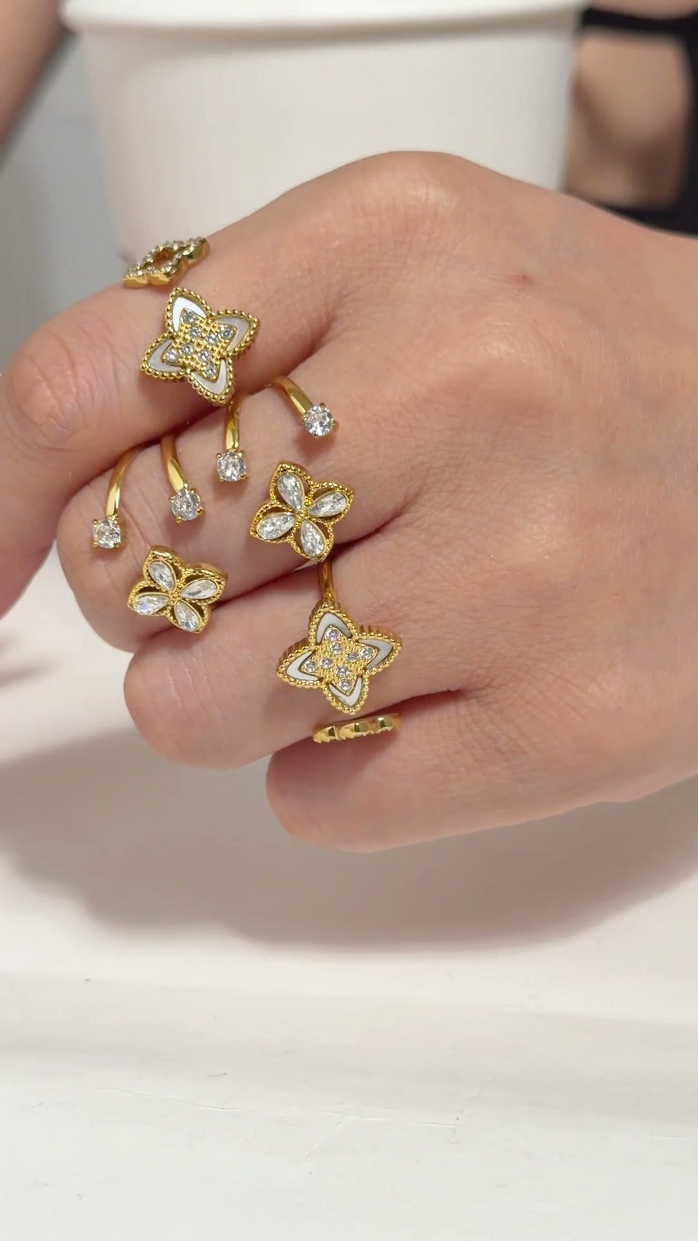 Gold-tone open bangles and rings with floral motifs and clear stone accents, shown on a model's hand and wrist.