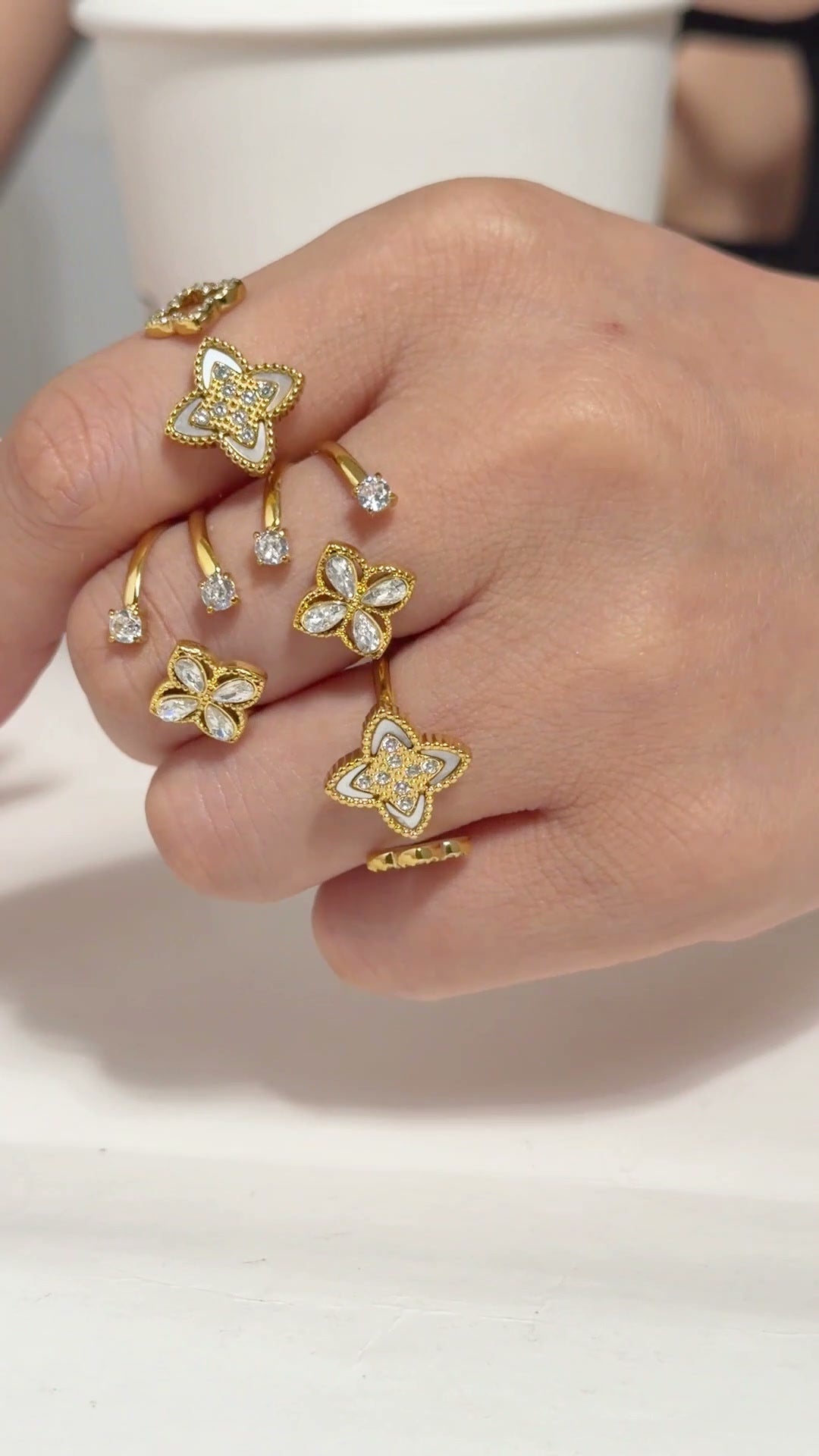 Gold-tone open bangles and rings with floral motifs and clear stone accents, shown on a model's hand and wrist.