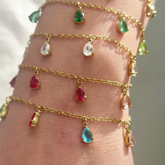 Delicate gold-tone chain bracelets with colorful teardrop-shaped dangling stones shown stacked on the wrist.