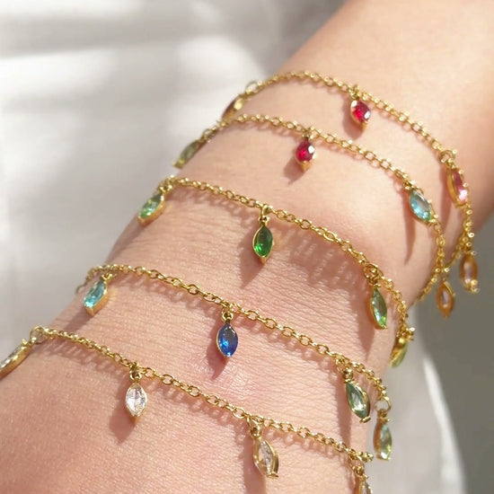 Gold-tone chain bracelets with colorful dangling stones shown layered on the wrist.