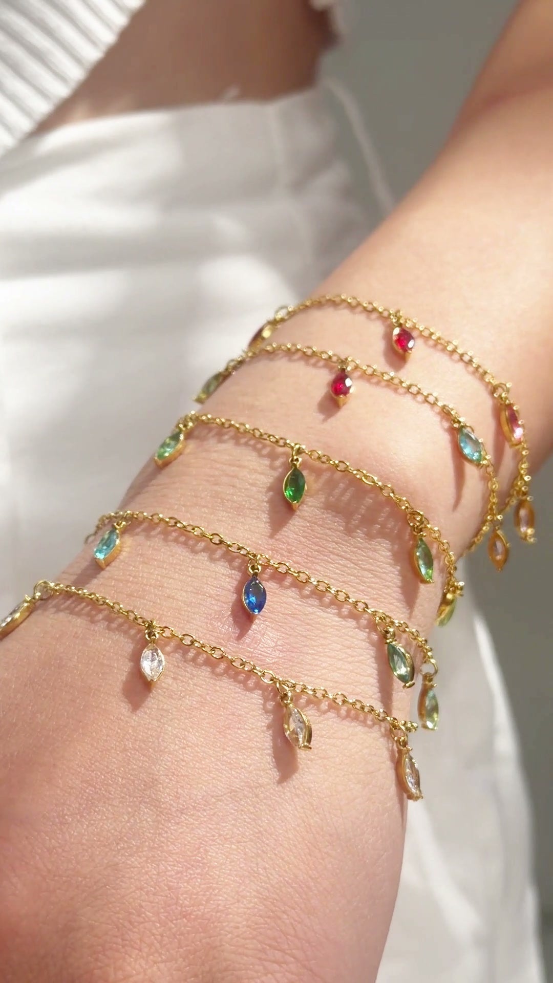 Gold-tone chain bracelets with colorful dangling stones shown layered on the wrist.