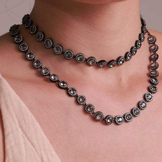 Layered black-tone necklaces with round smoky-colored stones and clear halo accents, shown on a model.