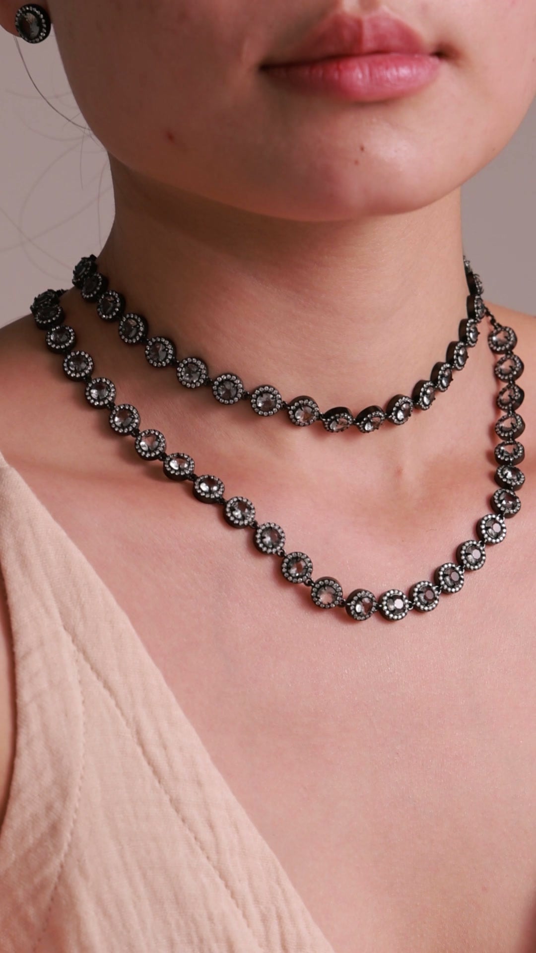 Layered black-tone necklaces with round smoky-colored stones and clear halo accents, shown on a model.